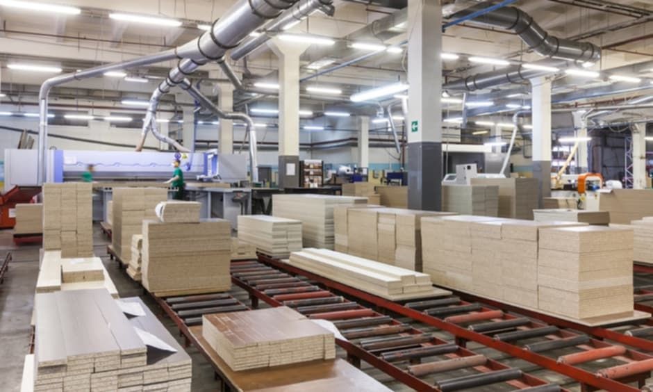 Large industrial warehouse with stacks of cardboard and machinery in the background, under bright fluorescent lighting.